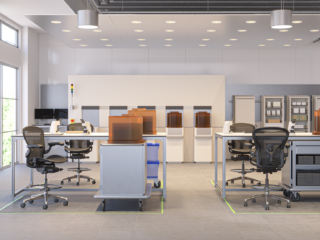 Tech lab with modular workbenches, mesh task chairs, rolling storage carts, and covered equipment units arranged in rows with shelving in the background.