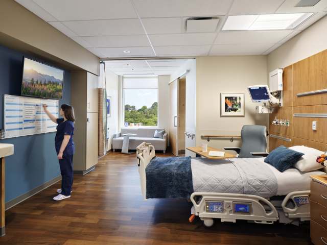Well-designed hospital room with new Healthcare Furniture digital board, patient bed, and family seating area. Modern patient suite with adjustable bed