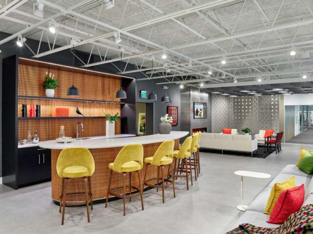 Lobby of CFI Workspace with a kitchenette and bar with yellow barstools. Couches and throw pillows.