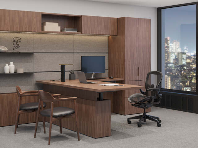 Executive office with L-shaped walnut desk, mesh task chair, two wood guest chairs, wall shelves, and built-in walnut storage against a city-view window.